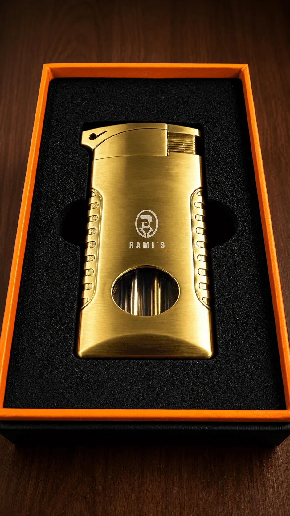 A "Rami's" Pipeliner cigar lighter with a luxurious brushed gold finish, presented in a black foam-lined display box with a vibrant orange border.