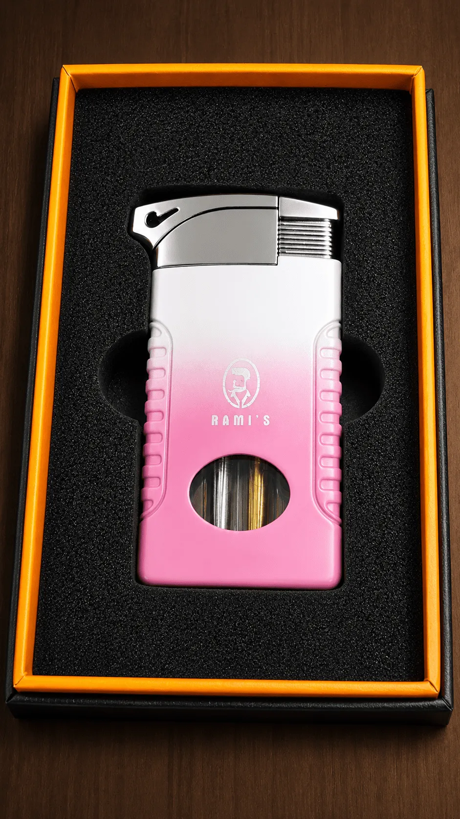 A white and pink gradient "Rami's" cigar lighter resting in a premium black and orange presentation box.