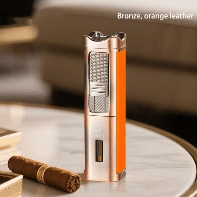 A tall bronze-finished Rami's Accessories executive lighter with vibrant orange leather siding, a fuel window, and integrated tools on a marble table.