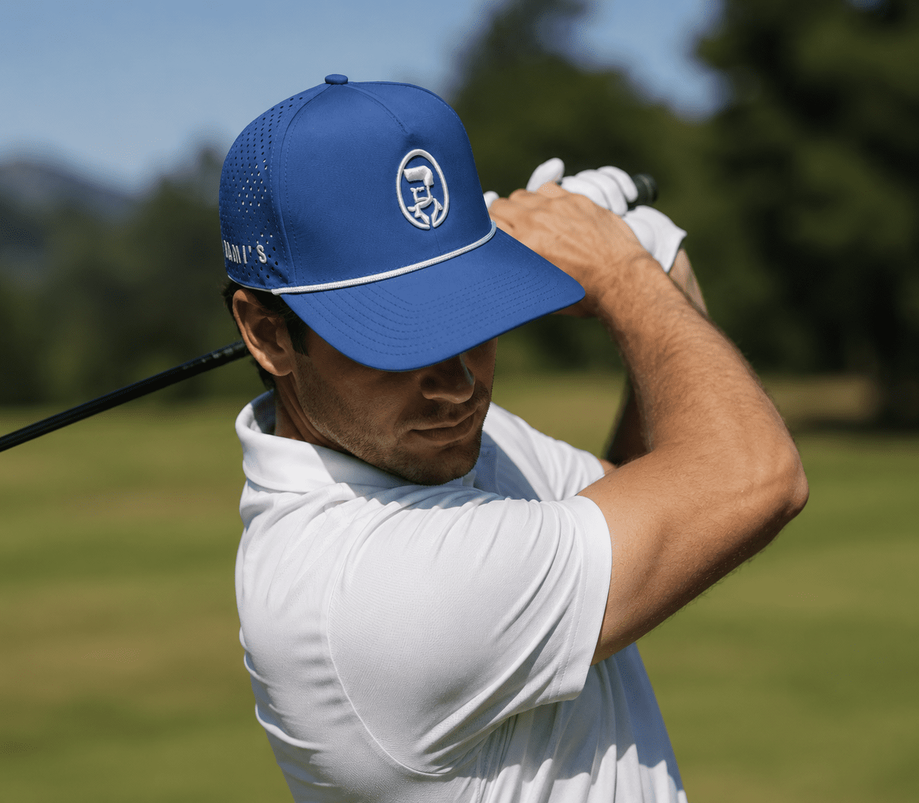 A golfer in a white polo wearing a bright cobalt blue Rami's Apex Performance Cap with a white rope detail on the brim and a circular white "Rami's" logo on the front, during a golf swing on a sunny course.