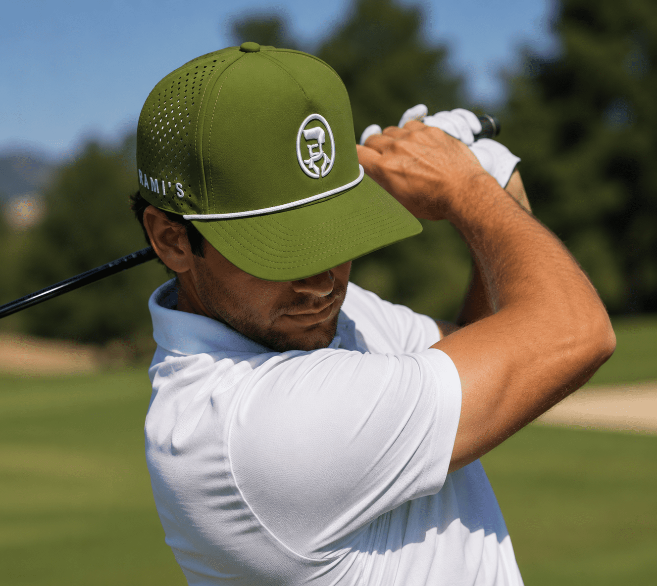 A golfer wearing a Rami's Apex Performance Cap in olive drab with a white rope detail on the brim and a circular white "Rami's" logo on the front, captured mid-swing on a golf course.