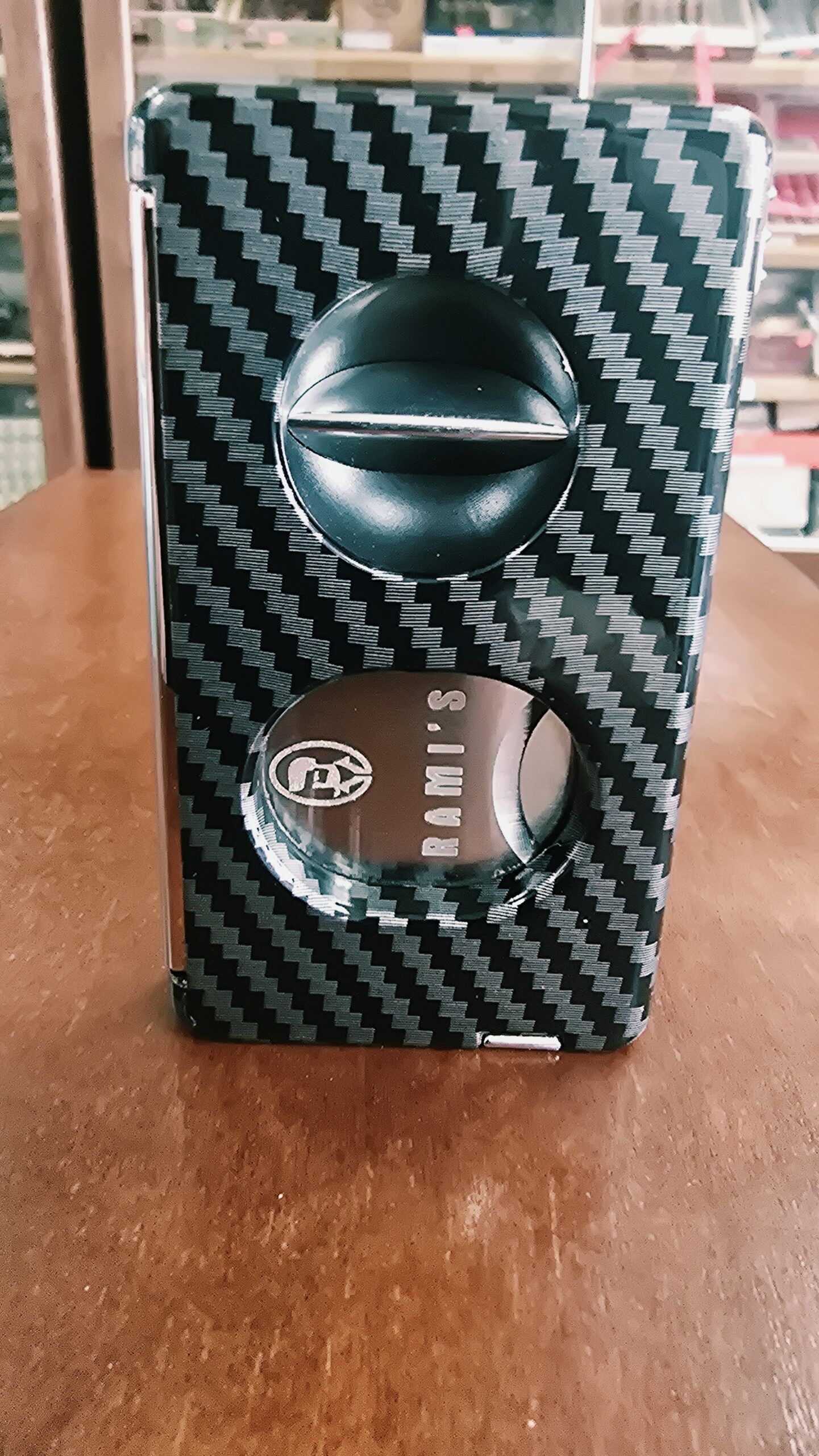 Rami's Carbon Elite Cutter displayed upright with a luxury carbon fiber finish, featuring an integrated V-cutter, guillotine cutter, cigar punch, and draw poker.
