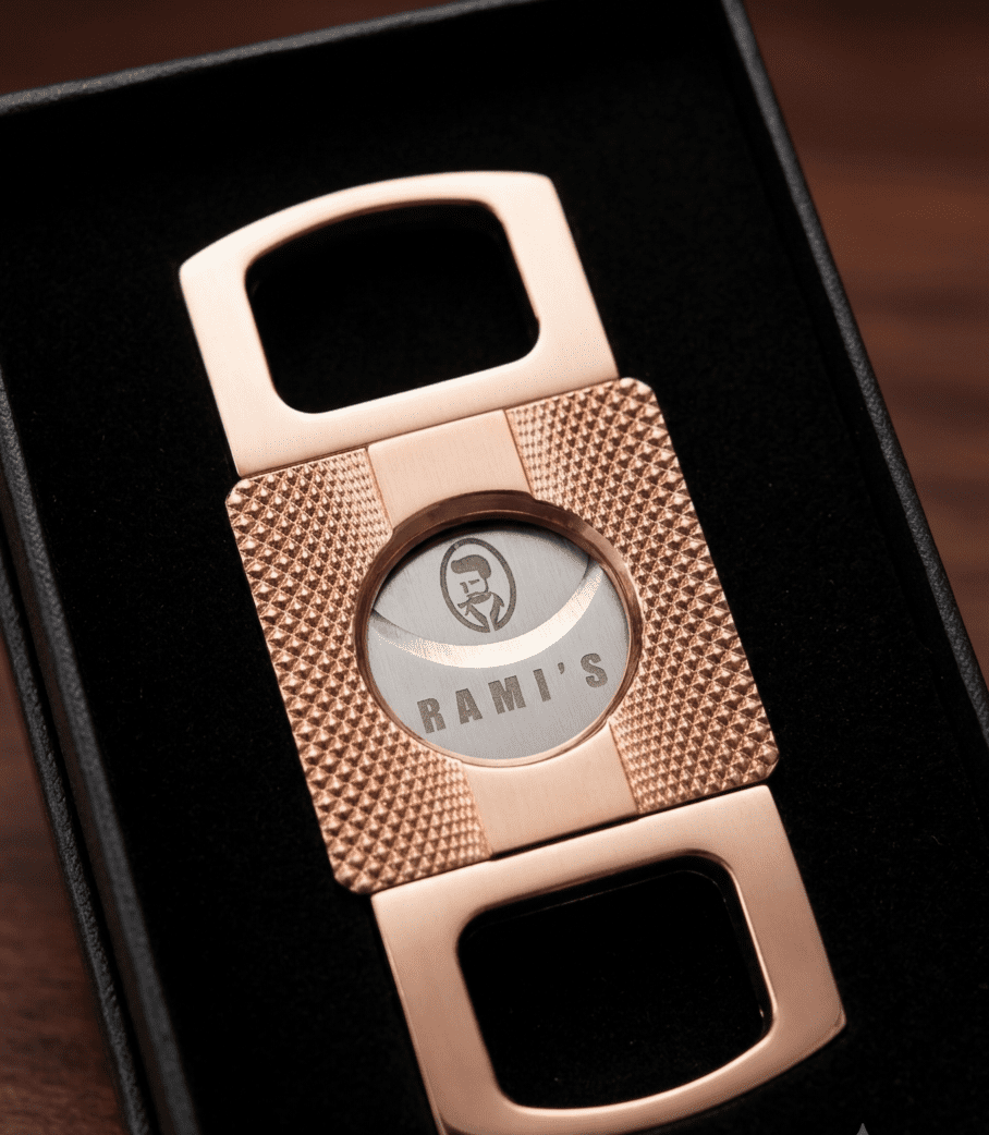 A close-up, high-angle shot of a rose-gold cigar cutter resting inside a black velvet-lined presentation box.