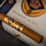 Diamond Crown Classic cigar resting on a closed wooden box with elegant gold and red branding.
