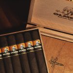 Open box of Olmec Maduro cigars, showcasing dark, oily wrappers and elegant presentation in a rustic, premium wooden box.