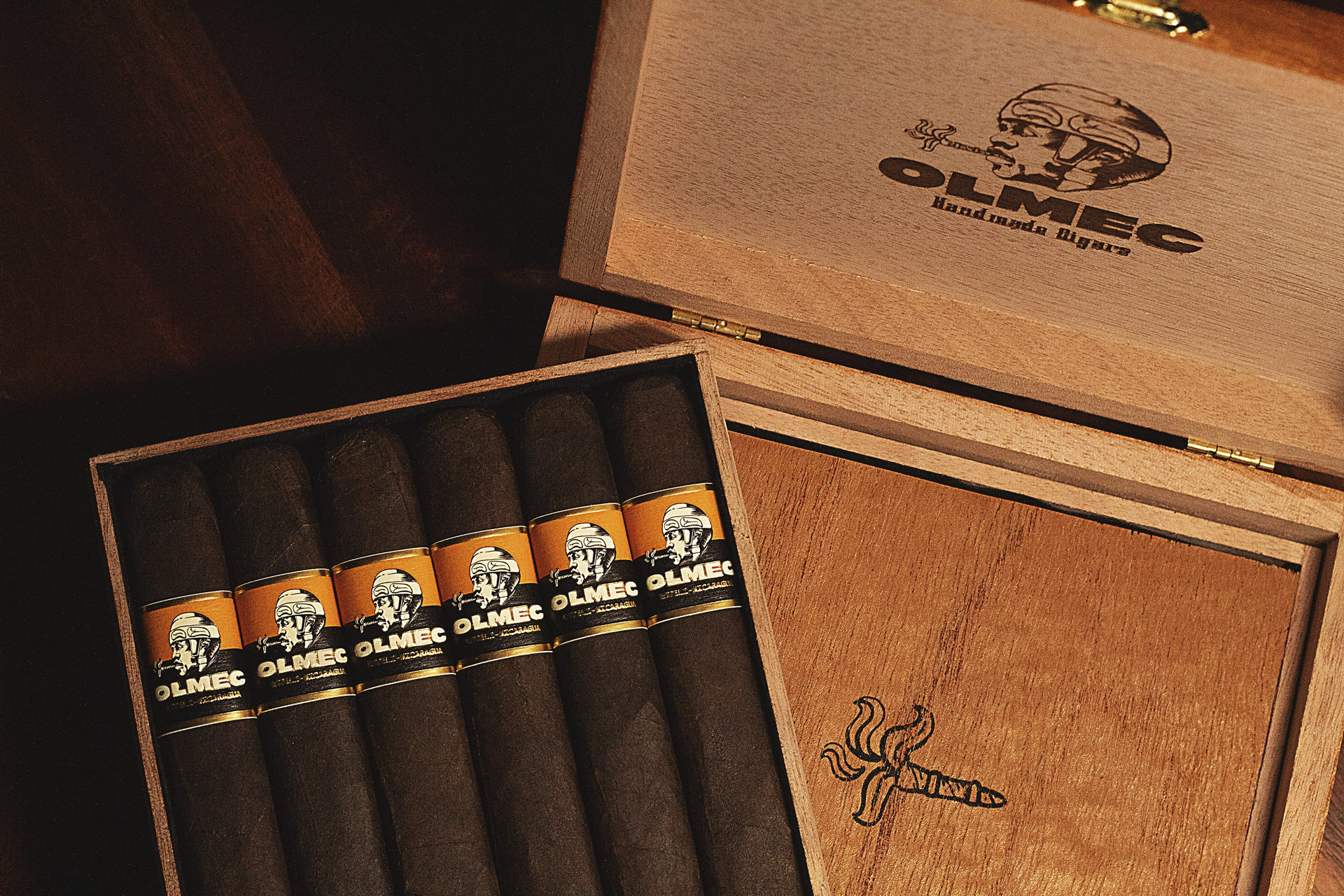 Open box of Olmec Maduro cigars, showcasing dark, oily wrappers and elegant presentation in a rustic, premium wooden box.