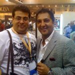 Rami Abou Daher, owner of Let's Smoke, standing alongside industry legend Rocky Patel at a premier cigar trade show, with the Oliva Cigar booth visible in the background.