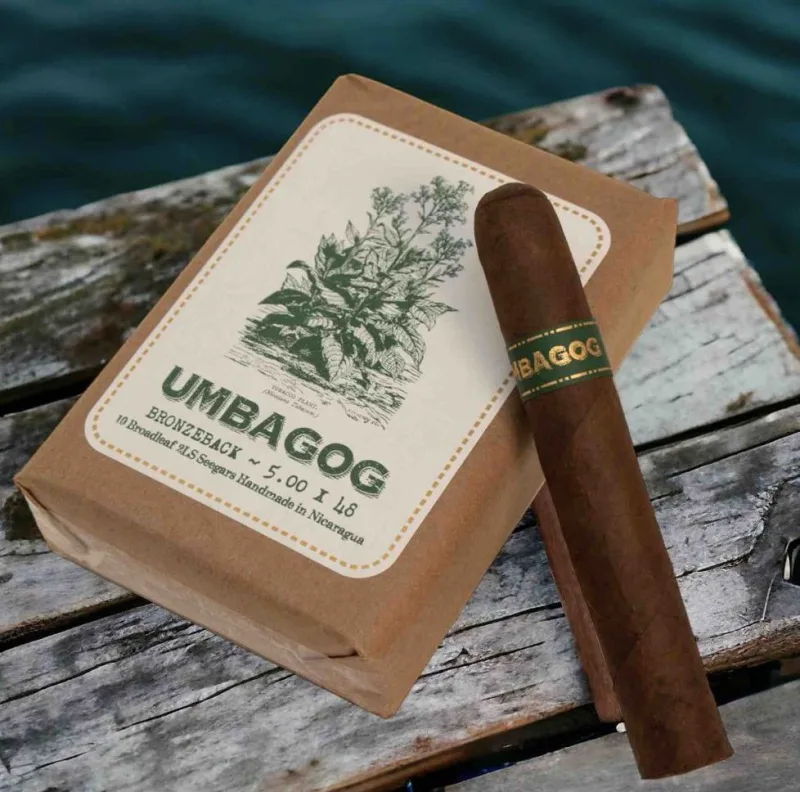 Single Umbagog cigar resting on a bundle of dark-wrapped cigars with rustic bands
