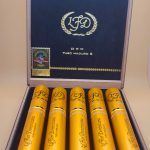 Open box of La Flor Dominicana Oro Tubo Maduro cigars, each housed in a sleek, shiny golden tube, arranged neatly inside a luxurious wooden box.