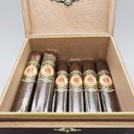 Open box of La Mission du L'Atelier 1959 cigars with dark San Andrés wrappers and elegant red-and-gold bands.