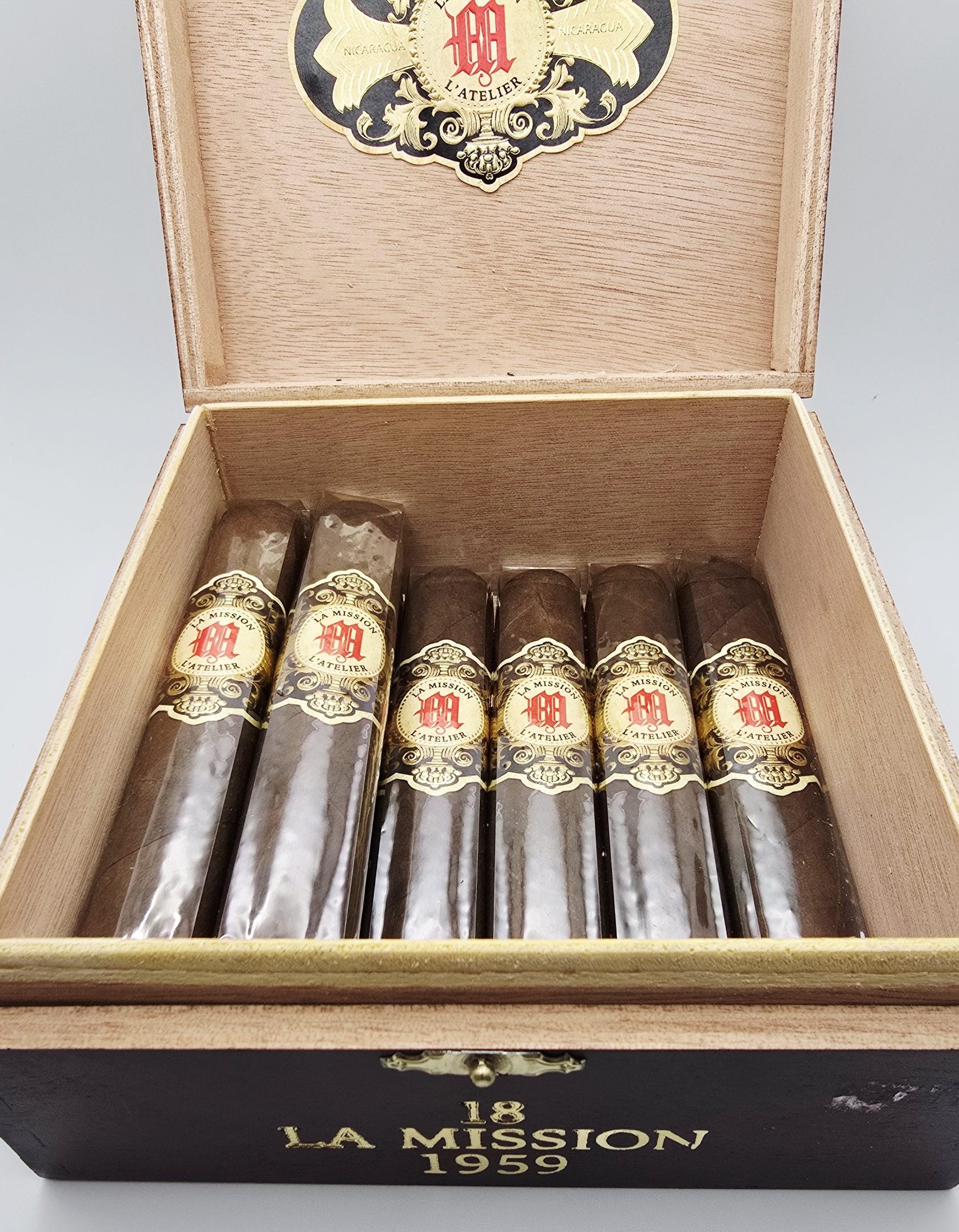 Open box of La Mission du L'Atelier 1959 cigars with dark San Andrés wrappers and elegant red-and-gold bands.