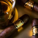 Three Partagás 1845 Clásico cigars arranged around a glass of cognac on a wooden surface.