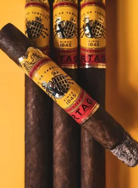 A lit Partagás Classic cigar resting on three unlit Partagás Classic cigars, with soft smoke rising.