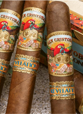 Three San Cristobal Revelation cigars with medium-brown wrappers and ornate bands resting diagonally on a closed wooden cigar box."