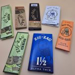 Various styles of Zig Zag Rolling Papers including Classic, Blue, and Organic, displayed with packaging.