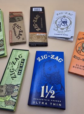 Various styles of Zig Zag Rolling Papers including Classic, Blue, and Organic, displayed with packaging.