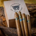 Three Guardian of the Farm cigars resting on the same box, showcasing their dark, rich wrappers and impeccable construction