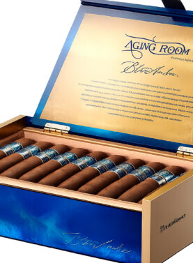 The file aging-room-blue-amber-open-box-jpg displays an open, luxury display box of Aging Room Quattro Nicaragua Blue Amber premium cigars, showcasing a vibrant blue lacquered exterior with gold accents, a metallic gold inner lid with branding script, and neatly arranged cigars with textured blue and silver bands