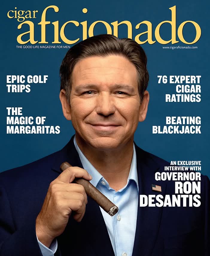 Cover of Cigar Aficionado magazine featuring Florida Governor Ron DeSantis holding a cigar while wearing a navy suit and light blue shirt. Headlines promote golf trips, cigar ratings, margaritas, blackjack tips, and an exclusive interview.