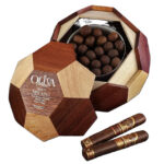 The file oliva-seriev-soccer-ball-melanio.jpg displays an open, soccer-ball-shaped wooden humidor box filled with round premium cigars, showcasing the Oliva Serie V Melanio Gran Reserva Limitada Double Toro Soccer Edition logo on the removable multi-toned wood lid alongside two cigars with specialized foot bands featuring a soccer ball icon.