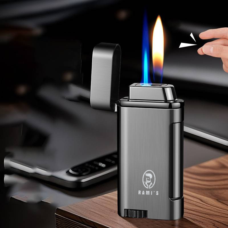 A gunmetal grey Rami's Accessories lighter with an open lid, displaying a unique dual flame consisting of a blue torch and a soft yellow flame, being activated by a hand snap.