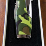 A "Rami's" Vanguard cigar lighter in a bold camouflage finish, featuring an integrated folding cigar knife with a locking mechanism, showcased in its presentation box.