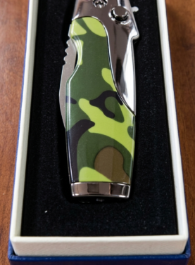 A "Rami's" Vanguard cigar lighter in a bold camouflage finish, featuring an integrated folding cigar knife with a locking mechanism, showcased in its presentation box.