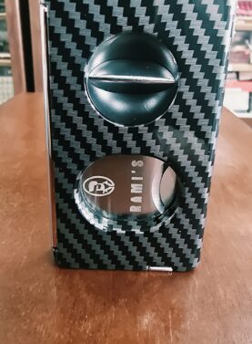 Rami's Carbon Elite Cutter displayed upright with a luxury carbon fiber finish, featuring an integrated V-cutter, guillotine cutter, cigar punch, and draw poker.