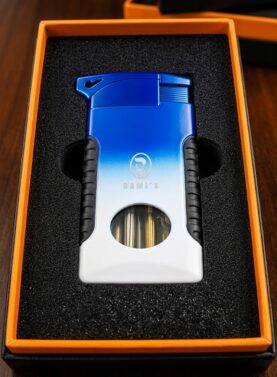 A "Rami's" Pipeliner cigar lighter with a bold blue-to-white gradient finish, presented in a black foam-lined display box with an orange inner border.