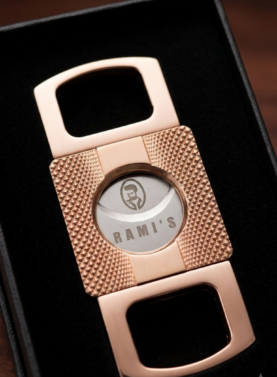 A close-up, high-angle shot of a rose-gold cigar cutter resting inside a black velvet-lined presentation box.